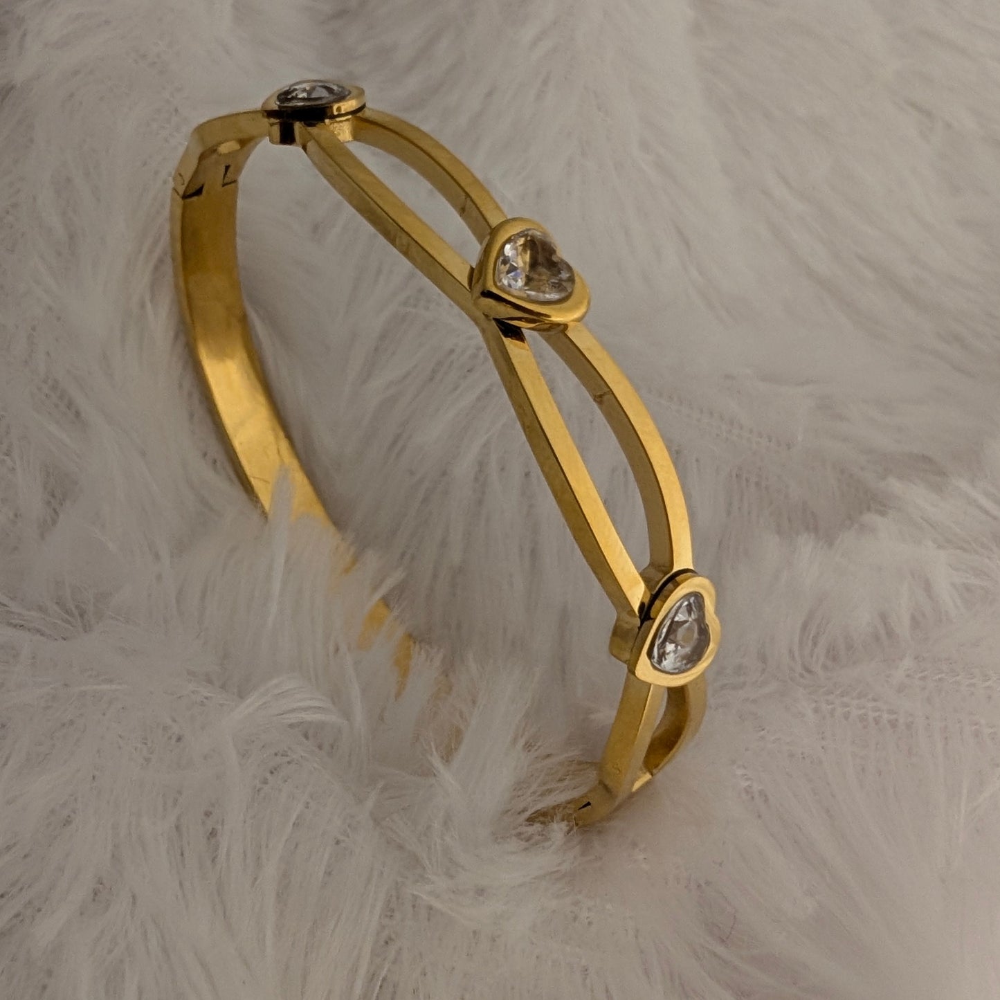 Gold bracelet with heart-shaped stones on a white feathered surface